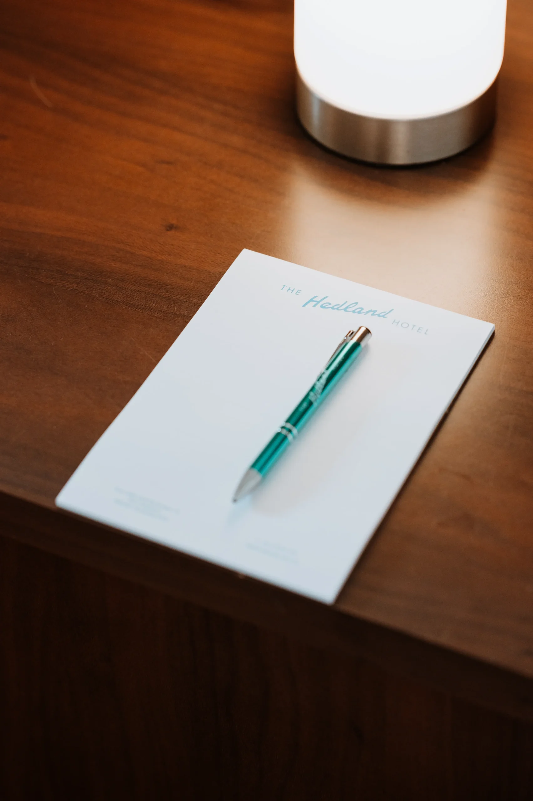 a close up of a pen and paper with The Hedland Hotel logo on the bedside table
