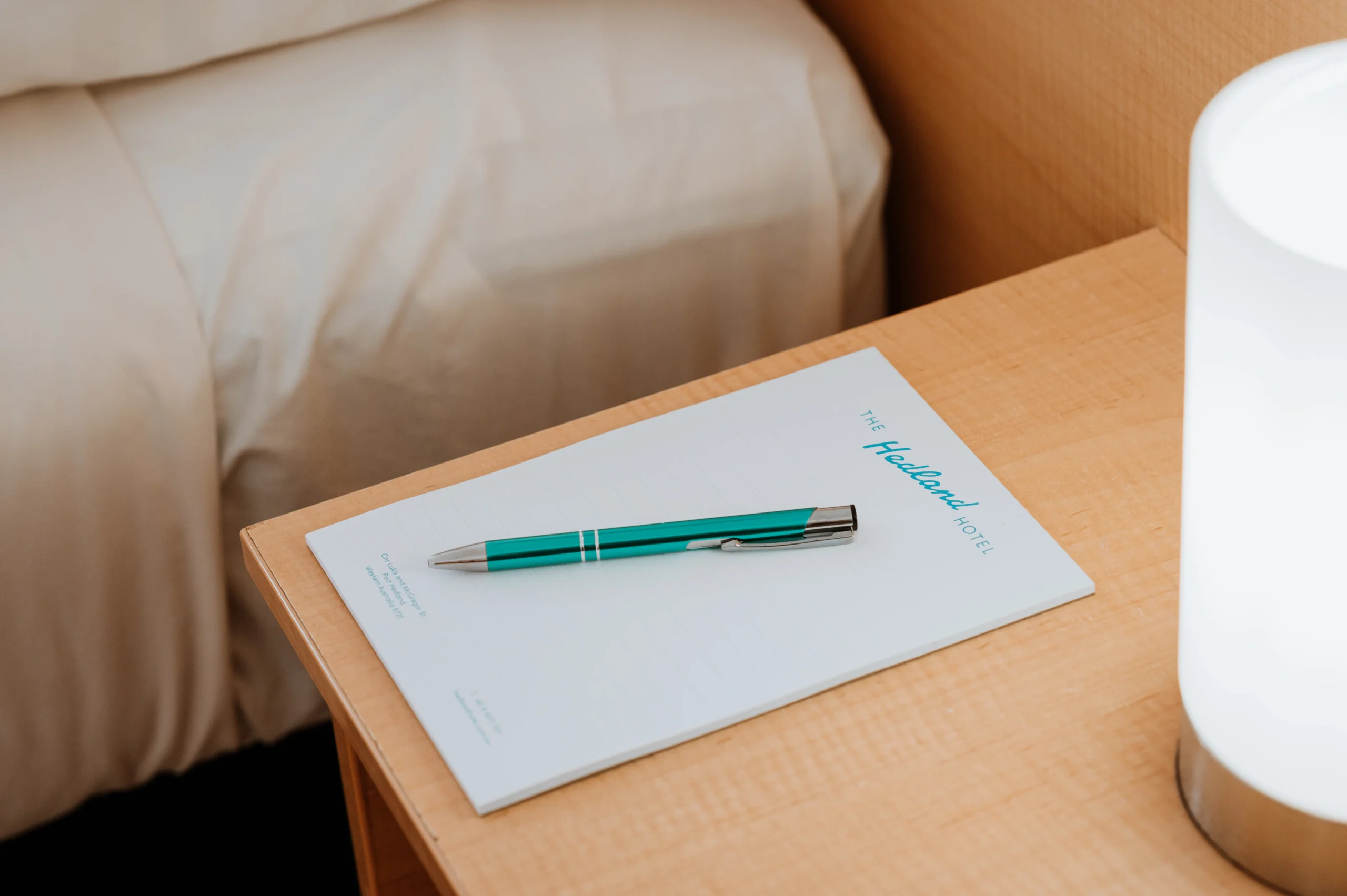 a close up of a pen and paper with The Hedland Hotel logo on the bedside table