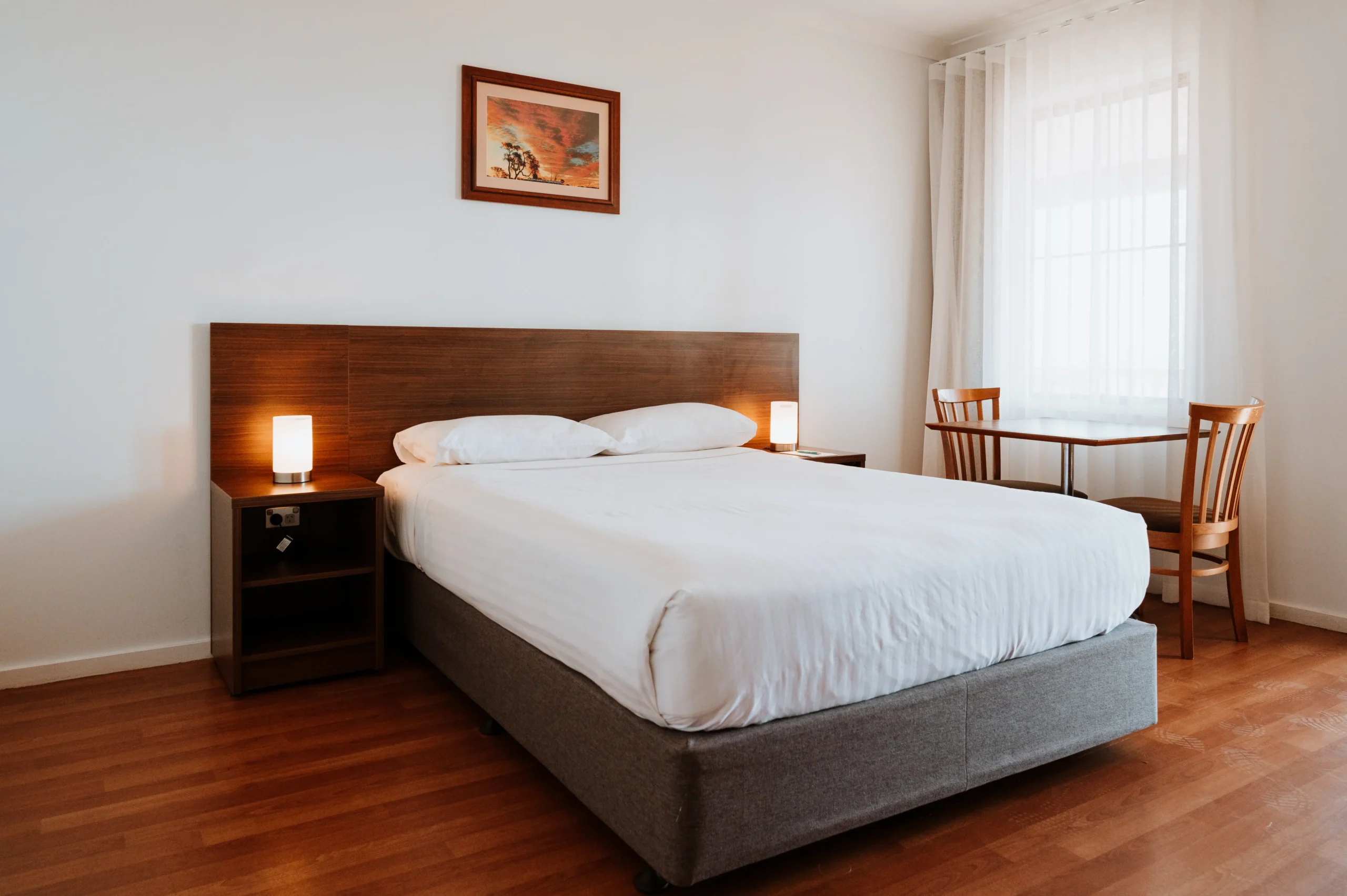 An interior photo of the Deluxe Room showing a clean white bed and bright window