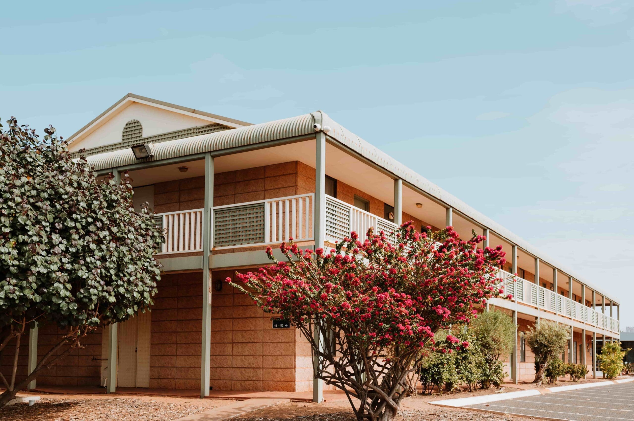 exterior view of rooms at The Hedland Hotel with wrap around terrace and native plants. The sun is shining and the day is bright