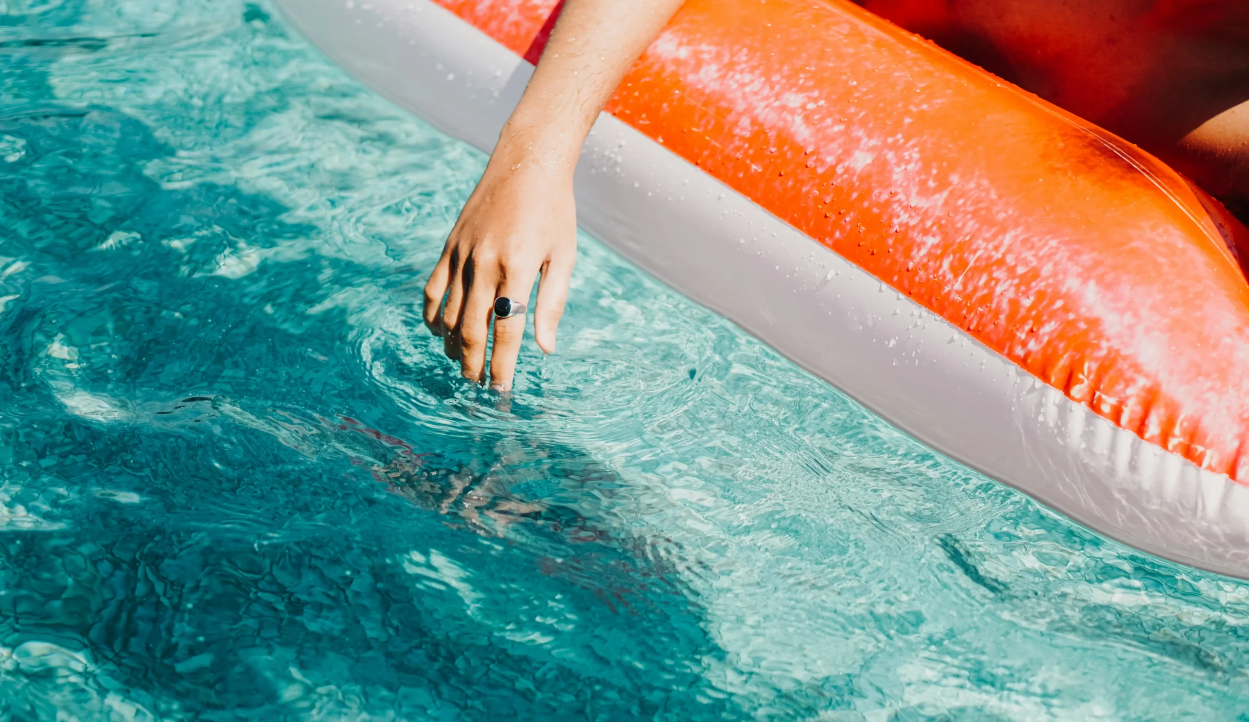 Close up of an inflatable pool toy with a female hand dipping into the water, the sun is shining